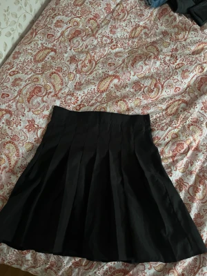 Svart plisserad kjol från SHEIN - Snygg svart kortkjol från SHEIN med plisserad design. Kjolen har en klassisk A-linjeform och är tillverkad i ett lätt och bekvämt material som passar perfekt till olika outfits. Dragkedja i sidan för enkel på- och avtagning.