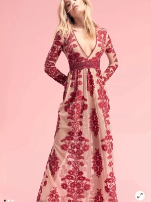  Maxi red Embroidered mesh dress - Romantisk långklänning i nude med röd broderad spets och blommigt mönster. Djup v-ringning, markerad midja och långa ärmar. Perfekt för dig som vill sticka ut med en elegant och unik look.