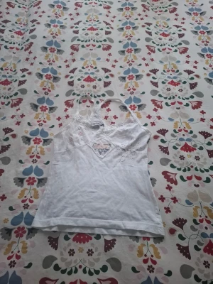 Vit linnetopp med spetsdetaljer - Söt vit linnetopp från Replay med tunna axelband och spetsdetaljer vid halsringningen. Toppen har broderade detaljer och en liten lapp framtill. Perfekt för en avslappnad och trendig look.