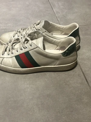 Gucci vita sneakers med röd/grön rand - Säljer ett par klassiska vita sneakers från Gucci med gröna och röda ränder. Säljer eftersom att de inte kommer till användning längre. De är äkta och köptes på plick för 3000 kr för några månader sedan. Mitt pris är förhandlingsbart vid snabb affär.