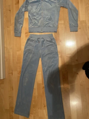 Ljus blå juicy couture set - Mysigt loungewear-set i ljusblå velour med dragkedja på tröjan och stora fickor på byxorna. Byxorna har resår i midjan och snörning samt bakfickor med knappar. Perfekt för chill dagar hemma.