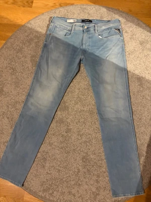 Ljusblå raka jeans från Replay Anbass - Säljer ett par ljusblå jeans från Replay med raka ben och klassisk femficksmodell. Jeansen har en snygg tvätt med lätt slitning framtill och bakfickor med diskret söm. Perfekta för en avslappnad och trendig look.