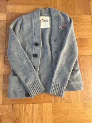 Sällsynt stickad vintage Hollister cardigan  - Tvärfet och väldigt sällsynt ljusgrå cardigan ifrån Hollister. Tröjan har en sjukt najs passform, 5 knappar, snygg design, och Hollister märket broderat i fin vinröd färg på bröstet. Storleken är S men passar snarare XS. Sjukt snygg cardigan, bra skick, inga defekter. Skriv vid eventuella frågor😁