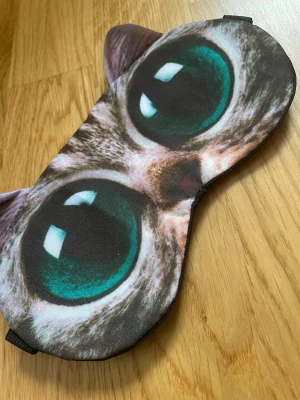 Sovmask med kattmotiv och öron - Rolig sovmask med stort kattansikte och 3D-öron. Masken har tryckta gröna kattögon och mjukt tyg som känns skönt mot huden. Perfekt för dig som vill ha en unik accessoar till sovstunden eller resan.