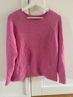 Rosa stickad tröja från Vero Moda - Snygg rosa stickad tröja från Vero Moda med rund halsringning och ribbade muddar vid ärmslut och nederkant. Tröjan har en mjuk och mysig känsla, perfekt för kyligare dagar. Enkel design som är lätt att matcha med olika outfits.