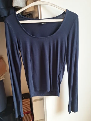 Mörkblå långärmad topp Gina Tricot - En enkel och stilren mörkblå långärmad topp från Gina Tricot. Toppen har rund halsringning och är tillverkad i mjuk bomullsmix som sitter skönt mot kroppen. Perfekt att matcha med jeans eller kjol för en clean look. Slitsade ärmar