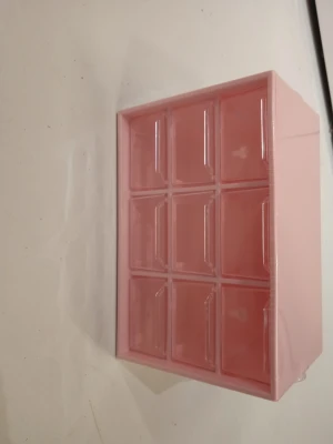 Rosa förvaringslåda med 9 fack - Säljer en rosa förvaringslåda i plast med nio små fack och transparenta lock. Perfekt för att organisera småprylar som smycken, pärlor eller kontorsmaterial. Lådan har hål på baksidan för enkel upphängning på väggen.