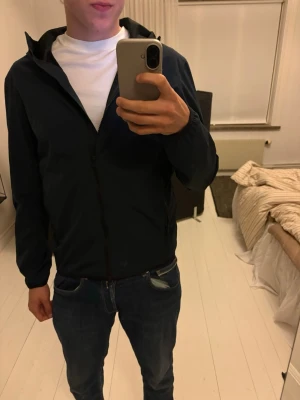 Mörkblå vindjacka från Colmar - Snygg svart vindjacka från Colmar med dragkedja framtill och huva. Jackan har diskret logga på ärmen och två sidofickor med dragkedja. Tillverkad i lätt och smidigt material som passar perfekt för blåsiga dagar. Modellen på bilderna är ca 180 och väger ca 80 kg, jackan är i storlek M