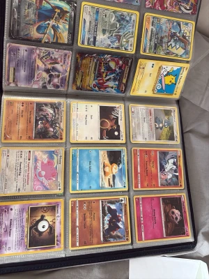 Pokémon Billz  - Stor samling Pokémonkort i en svart pärm med plastfickor. Innehåller blandade kort med olika Pokémon, färger och energityper, inklusive både vanliga och holografiska kort. Perfekt för samlare eller dig som vill utöka din kortlek.