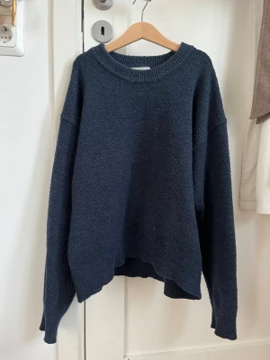 Mörkblå  stickad tröja - Mysig mörkblå stickad tröja med  passform och rund halsringning. Tröjan har långa ärmar och är tillverkad i ett mjukt, fluffigt material som ger en avslappnad look. Perfekt för lager på lager och chill dagar.