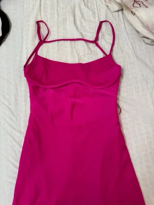 Rosa ärmlös klänning med smala band - Säljer en snygg rosa klänning med smala axelband och figurnära passform. Klänningen har en enkel, stilren design och är tillverkad i ett mjukt, slätt material som ger en skön känsla. Perfekt för dig som vill sticka ut med färg!