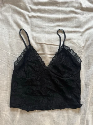 Svart spetstopp  - Säljer en svart topp från BikBok med tunna axelband och vacker spetskant vid urringningen. Hör av dig vid frågor ❤️