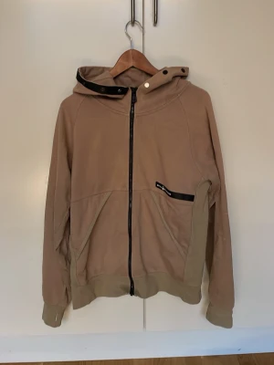 Beige hoodie från Sailracing  - Säljer en beige hoodie från Sailracing med dragkedja framtill, huva med svart kant och knappdetalj samt två fickor. Materialet känns mjukt och skönt, perfekt för chill dagar. Diskret logga på huvan och svart detalj på bröstet. Nypris 1800kr hör av er vid minsta fundering mvh Artur !