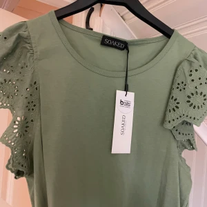 Grön blus med broderade ärmar Soaked - Supersöt ljusgrön/khaki blus från Soaked in Luxury. volanger på axlarna och broderier i blom mönster. Oanvänd, inköpt för 499kr! Inga defekter!  100% bomull