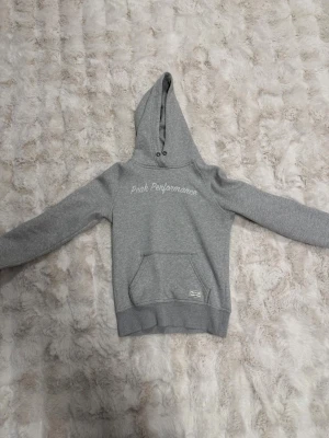 Grå hoodie från Peak Performance - Säljer en grå hoodie från Peak Performance med broderad logga på bröstet. Hoodien har en klassisk känguruficka framtill, ribbade muddar och dragsko i huvan. Tillverkad i mjukt sweatshirtmaterial som är perfekt för chill dagar. Priset kan diskuteras 