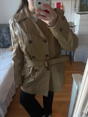 Vintage läder trenchcoat skinnjacka - beige /camel - Albacken Malmö - Vintage trenchcoat i äkta läder Jackan är Made in Sweden och har en klassisk dubbelknappt trench-design med balte i midjan som ger en snygg och tidlos siluett. Färgen är beige / camel, vilket gör den lätt att matcha till både vardag och mer uppklädda outfits. Står ingen storlek, men man kan dra åt bandet så den passar efter sin figur. Jag bär vanligtvis M-L, och är 164cm  Perfekt för hösten, våren eller en minimalistisk capsule wardrobe. Knapparna ar lite lösa som man kan sy ihop sjalv