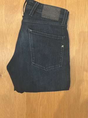 Mörkblå från Replay - Säljer ett par mörkblå jeans från Replay med klassisk femficksmodell och diskret logga på bakfickan. Jeansen har smal passform och är tillverkade i stretchigt denimtyg för extra komfort. Perfekta för en trendig och avslappnad look.