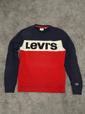 Levi's färgblockad sweatshirt - Snygg sweatshirt från Levi's med färgblock i marinblått, rött och vitt. Stor logga framtill, rund halsringning och långa ärmar. Tillverkad i mjuk bomullsblandning för skön känsla. Perfekt för en avslappnad streetwear-look.