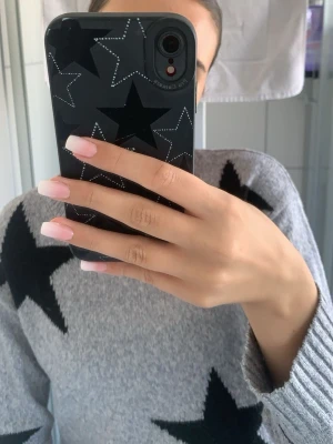 Grå stickad tröja med svarta stjärnor - Säljer en grå stickad tröja med stora svarta stjärnor som mönster. Tröjan har rund halsringning och långa ärmar. 