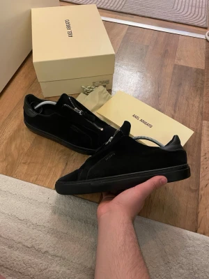 Svarta sneakers Axel Arigato zip 90 - Svarta sneakers från Axel Arigato i mocka med unik dragkedja framtill istället för klassiska snören. Snygg minimalistisk design med låg profil och diskret logga på sidan. Perfekta för dig som gillar stilrena och moderna skor. Storlek 41 passar   42