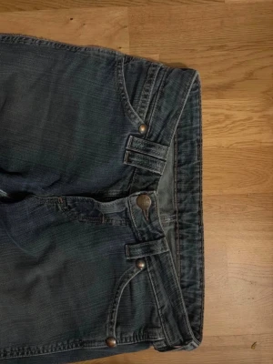 Mörkblå lågmidjade bootcut jeans med detaljer - Säljer ett par mörkblå bootcut & low rise jeans med slitningar och unika dubbla bälteshällor framtill och ett hål i höger knä. De är väldigt bekväma och snygga! Storlek: W:28 L:32 Men passar mig som har 36/S vanligtvis. Skriv gärna privat för mer information 🥰