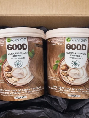 Garnier Good hårfärg vegansk - Två burkar Garnier Good hårfärg i nyansen 7.3, en varm ljusbrun ton. Förpackningarna är runda med beige lock och har illustrationer av hår och naturliga ingredienser. Vegansk formula och 100% täckning av grått hår. Perfekt för dig som vill ha ett naturligt resultat.