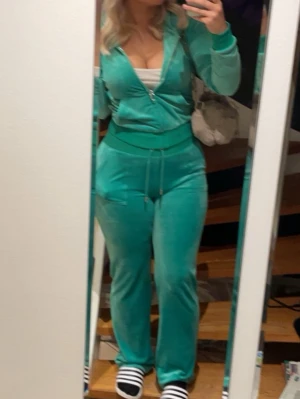 Grön velour loungewear-set Juicy Couture - (Byxorna är i storlek M och tröjan i storlek S)Snyggt och klassiskt loungewear-set från Juicy Couture i mjuk grön velour. Setet består av en zip-hoodie med fickor och matchande byxor med raka ben och dragsko i midjan. Perfekt för chill dagar hemma eller när du vill vara bekväm men ändå se trendig ut.
