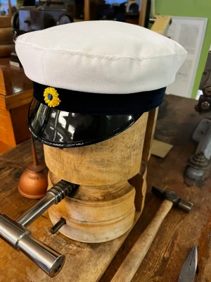 Studentmössa med svart skärm - Klassisk studentmössa med vit ovandel, blått band och blank svart skärm. Framtill sitter en gulblå kokard som detalj. Perfekt accessoar till studenten och tillverkad i tyg och plast. Typisk svensk design.