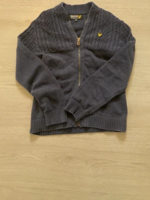 Mörkblå ziptröja från Lyle & Scott - Mörkblå stickad ziptröja från Lyle & Scott med gul logga på bröstet. Tröjan är i storlek 12-13 och har inga defekter eller några fläckar. (Priset är ej hugget i sten). 
