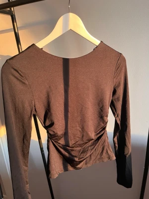 Svart långärmad topp med öppen rygg - Snygg svart långärmad topp med en unik öppen rygg-detalj. Toppen har en tight passform och är tillverkad i ett stretchigt syntetmaterial som ger en smickrande siluett. 