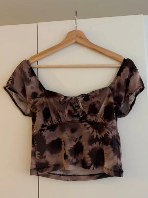 Brun mönstrad topp med snörning - Säljer en croppad topp i bruna och beige toner med coolt abstrakt mönster. Passar en mindre kupa. 