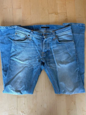 Ljusblå jeans från Nudie Jeans - Säljer ett par ljusblå jeans från Nudie Jeans med raka ben. Perfekta för en avslappnad och trendig stil. Modellen är Grim Tim. W29/L32