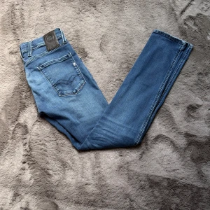 Blå jeans från Replay  - Snygga blå Repaly anbass jeans med klassisk femficksdesign och läderpatch bak i midjan. Jeansen har raka ben och tydliga kontrastsömmar. Tillverkade i mjuk denim med lätt tvättad look och subtila slitningar. W29 L32