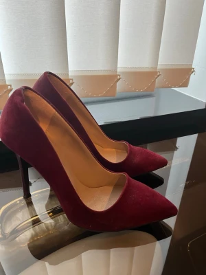 Vinröda pumps i mocka - Snygga vinröda pumps med spetsig tå och hög klack. Skorna är tillverkade i mjuk mocka och har en elegant siluett som ger en trendig look. Perfekta för dig som vill sticka ut med färg och stil.