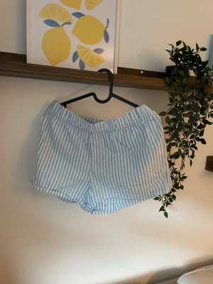 Blåvitrandig shorts i bomull - Säljer ett par blåvitrandiga shorts med relaxed fit och elastisk midja. Shortsen är tillverkade i mjuk bomull och har en klassisk, enkel design som passar perfekt till sommaren.