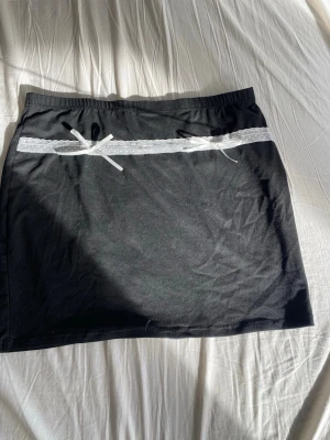 Svart kortkjol med spetsdetalj - Svart kortkjol med vit spets och rosett framtill, så söt men tyvärr för stor för mig, passar som både lådmidjad till högmidjad 🦎