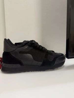Svarta sneakers från Valentino - Säljer ett par svarta sneakers från Valentino med i mocka, läder och mesh. Skorna har en chunky sula och klassisk snörning. Perfekta för dig som vill ha en stilren och edgy look till vardagsoutfiten. 