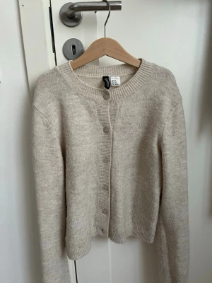 Beige kofta från H&m - Mysig beige kofta från h&m med rund halsringning och knappar framtill. Koftan har lång ärm, ribbade muddar och är tillverkad i ett mjukt, stickat material. Perfekt att slänga över en topp för en enkel och clean look.