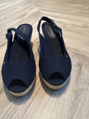 Marinblå kilklackssandaler Tommy Hilfiger - Snygga marinblå sandaler från Tommy Hilfiger med öppen tå och kilklack i flätad jute. Justerbar rem med spänne runt hälen och diskret logga på sidan. Ovandel i tyg och klassisk espadrille-look som ger en trendig vibe.