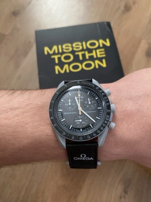 Omega X Swatch Mission To The Moon Gold Needle - Säljer en Omega x Swatch Speedmaster MoonSwatch med svart urtavla och svart textilband. Klockan har kronograf, tachymeter och tydliga vita visare. Levereras i originalförpackning från Bioceramic MoonSwatch Collection.