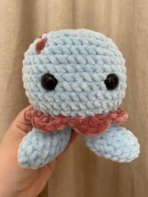 Handvirkad bläckfisk i mjuk chenille – ca 14 cm - Handvirkad bläckfisk i supermjukt chenillegarn med fina detaljer och stora säkerhetsögon. En söt och kramvänlig liten plushie som passar perfekt som present eller inredningsdetalj. Varje exemplar är unikt och gjort helt för hand. Ca 14 cm hög.