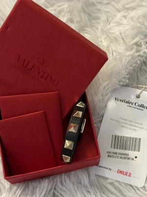 Valentino Garavani  - Snyggt svart armband från Valentino i äkta läder med ikoniska guldfärgade pyramidnitar. Justerbart spänne för perfekt passform. Kommer i original röd box, valentino äkta bevis kuvert och med tagg från Vestiaire Collective. 