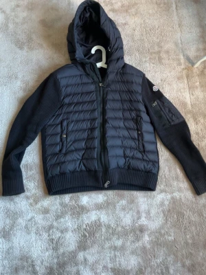Moncler Cardigan - Snygg svart cardigan från Moncler i strlk S med stickade ärmar och quiltad front. Jackan har huva, dragkedja framtill, ribbade muddar och fickor med dragkedja. Perfekt för kalla dagar och har en modern, sportig look. 