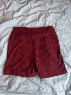 Mörkröda ribbade shorts - Snygga mörkröda shorts med ribbad struktur och bred resår i midjan. Perfekta för en avslappnad och trendig look. Materialet känns mjukt och stretchigt, vilket gör dem riktigt bekväma att bära.