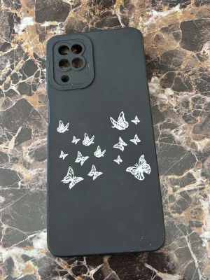 Svart mobilskal med vita fjärilar Samsung A12 - Snyggt svart mobilskal med vita fjärilar på baksidan. Skalets material är mjukt silikon som ger bra grepp och skydd. Passar en mobil med fyrkantigt kamerahål och flera linser. Perfekt för dig som vill ha ett stilrent men ändå personligt skal. För samsung A12