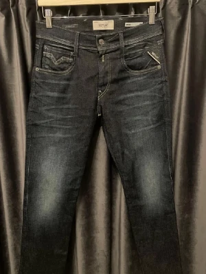 Replay anbass jeans - Snygga svarta slim fit jeans från Replay med Hyperflex-material som ger extra stretch och komfort. Klassisk femficksmodell med diskreta slitningar och tydliga sömmar. Perfekta för dig som gillar en modern och stilren look. Storlek: 28,30