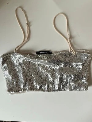 Silvrig paljettlinnetopp Gina Tricot - Glittrig silvrig linnetopp från Gina Tricot med tunna justerbara axelband. Toppen är täckt av paljetter och har en croppad passform som passar perfekt till festliga tillfällen.