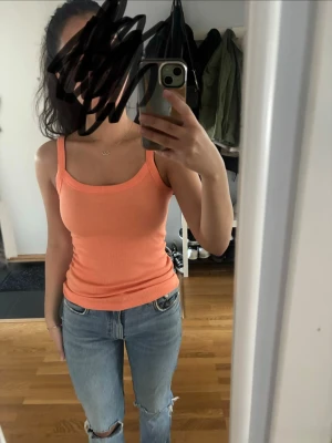 Ribbad orange linnetopp - Snygg ribbad orange linnetopp med smala axelband och figurnära passform. Perfekt för varma dagar och enkel att styla med jeans eller kjol. Mjuk och stretchig känsla.