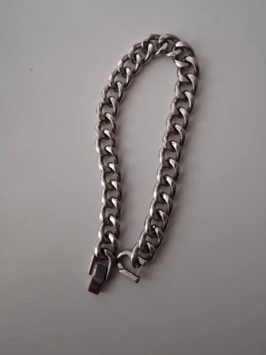 Tungt silverfärgat kedjearmband - Snyggt och robust armband i silverfärgad metall med breda, tätt sammanlänkade länkar. Armbandet har en kraftig låsdetalj och en stilren, minimalistisk design som passar till många olika stilar. Perfekt för dig som gillar chunky accessoarer.