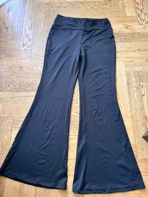 Svarta utsvängda mjukisbyxor  - Svarta mjukisbyxor  med utsvängda ben och hög midja. Tillverkade i ett mjukt och stretchigt material som sitter skönt på kroppen. Perfekta för en avslappnad och trendig stil.